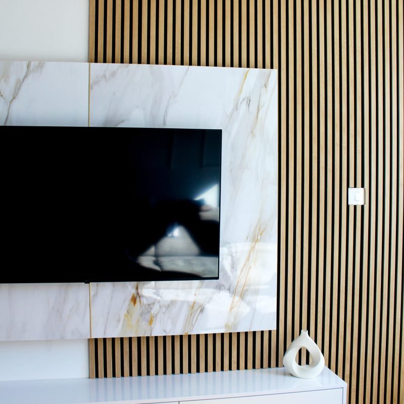 Wall-mounted TV on marble background with warm LED backlight and wooden accent wall for a modern interior look.